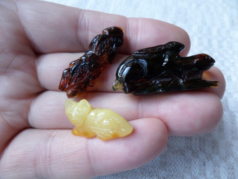 May include: Three amber carvings of animals. A brown and black rabbit, a brown and black dragon, and a yellow cat.