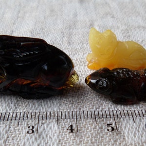 May include: Two amber carvings of animals. One is a dark brown frog, the other is a light yellow cat. Both are about 2 inches long.
