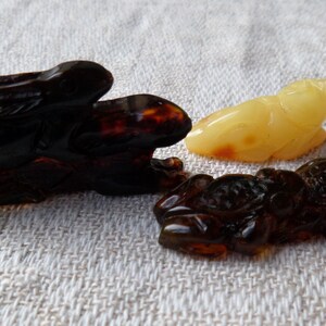May include: Three amber animal carvings: a dark brown rabbit, a light brown frog, and a light yellow frog. The carvings are detailed and intricate.