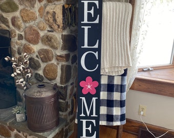 May include: Black wooden welcome sign with white lettering spelling "WELCOME" and a pink flower graphic. The sign also says "Family & Friends" in white cursive lettering.