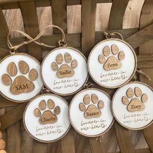 May include: Six wooden ornaments with paw prints and the names Sam, Sadie, Zena, Baxter, Zoey, and Charlie. Each ornament has the text "forever in our hearts".