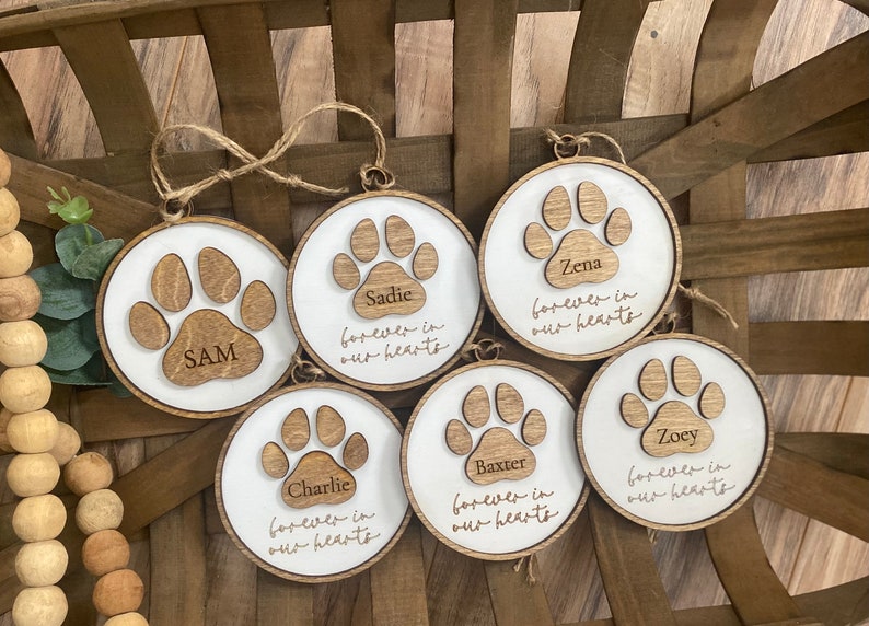 May include: Six wooden ornaments with paw prints and the names Sam, Sadie, Zena, Baxter, Zoey, and Charlie. Each ornament has the text "forever in our hearts".