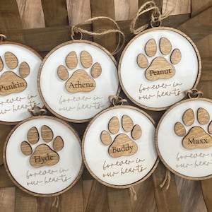 May include: Six wooden ornaments with paw prints and the names Punkin, Athena, Peanut, Hyde, Buddy, and Maxx. Each ornament has the text "forever in our hearts".