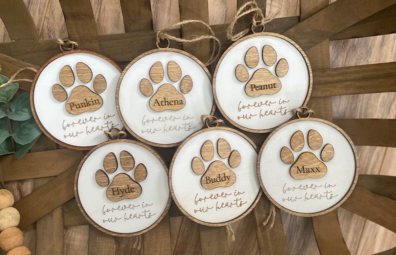 May include: Six wooden ornaments with paw prints and the names Punkin, Athena, Peanut, Hyde, Buddy, and Maxx. Each ornament has the text "forever in our hearts".