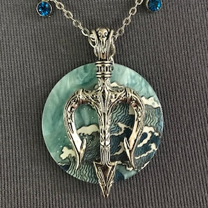 Puede incluir: Collar con colgante de tridente plateado y fondo circular con tem&aacute;tica oce&aacute;nica. El colgante presenta un dise&ntilde;o de tridente detallado. El collar incluye dos peque&ntilde;os acentos de piedras preciosas azules en la cadena.