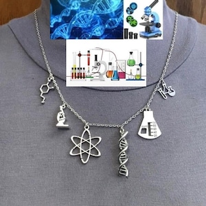 Op de afbeelding: Zilverkleurige ketting met wetenschappelijke bedels, waaronder een microscoop, atoom, DNA-helix en laboratoriumglaswerk. De ketting wordt getoond tegen een grijze achtergrond, met wetenschappelijke illustraties op de achtergrond.