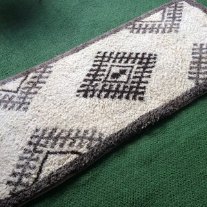 May include: A white and brown patterned rug with a geometric design. The rug has a fluffy texture and is made of wool.