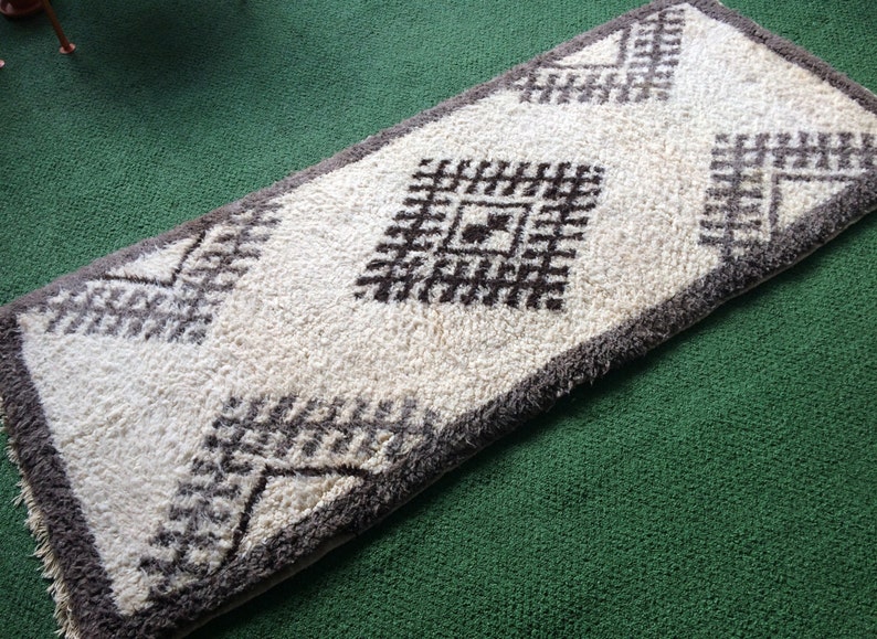 May include: A white and brown patterned rug with a geometric design. The rug has a fluffy texture and is made of wool.