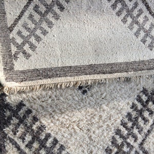 May include: Two white rugs with a geometric pattern in brown. The top rug has a fringe border.