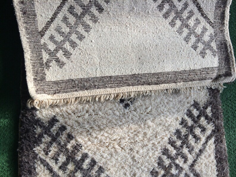 May include: Two white rugs with a geometric pattern in brown. The top rug has a fringe border.