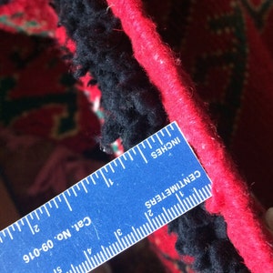 May include: Close-up of a red and black rug with a blue ruler measuring 2 inches. The ruler has the text "Cat No. 06-016", "CENTIMETERS", and "INCHES" printed on it.