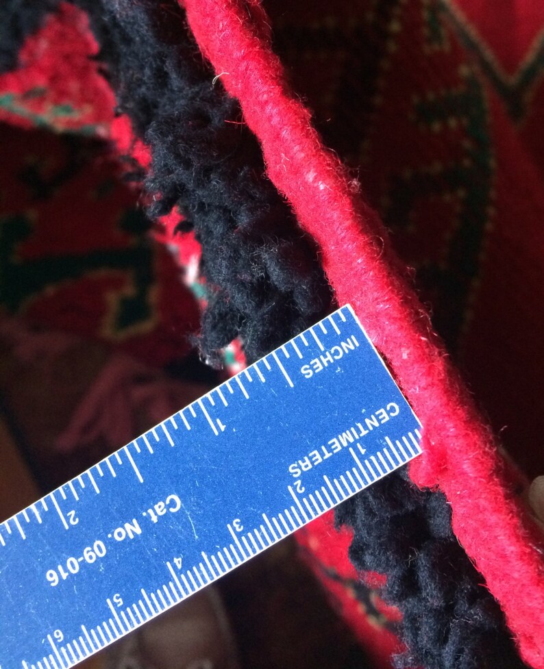 May include: Close-up of a red and black rug with a blue ruler measuring 2 inches. The ruler has the text "Cat No. 06-016", "CENTIMETERS", and "INCHES" printed on it.
