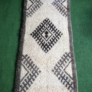 May include: A white rug with a brown geometric pattern. The rug has a fringe border and is made of a soft, fluffy material.