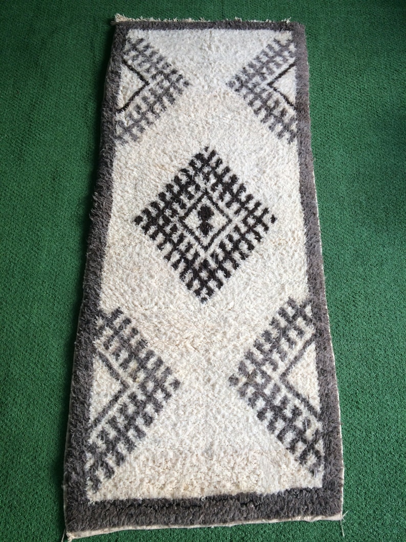 May include: A white rug with a brown geometric pattern. The rug has a fringe border and is made of a soft, fluffy material.