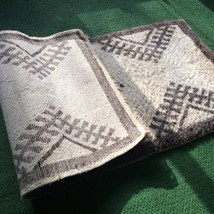 May include: A white and brown patterned rug with a geometric design. The rug is folded in half and is lying on a green surface.