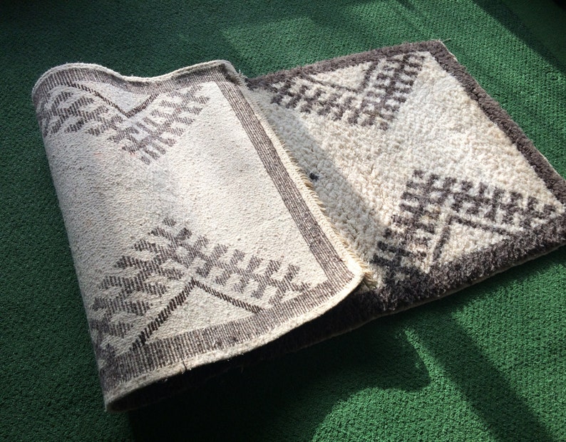 May include: A white and brown patterned rug with a geometric design. The rug is folded in half and is lying on a green surface.