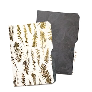 May include: A white folder with a gold fern pattern on the front and a black folder with a subtle pattern on the back.