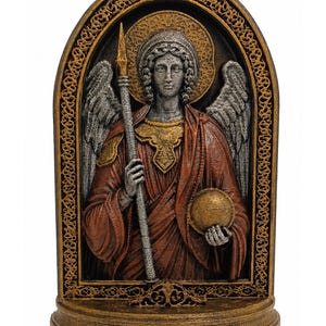 May include: A relief sculpture of an angel figure holding a tall spear and a sphere. The figure has silver wings, a gold halo, and wears a dark red robe. The entire piece is framed by an arched, ornate gold border on a solid base.