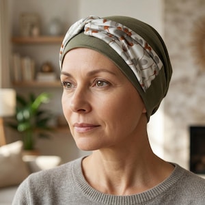 May include: Olive green head covering with a floral patterned band. The head covering is made of soft fabric and is designed to be comfortable. The floral pattern includes white, brown, and gray elements. The head covering is worn by a person.