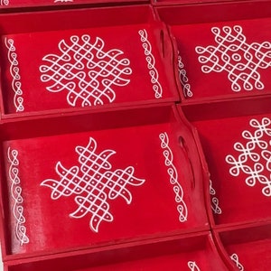 Pode incluir: Conjunto de seis bandejas de madeira vermelhas com desenhos intrincados brancos. As bandejas têm uma borda decorativa e uma alça de cada lado.