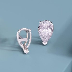 May include: A pair of silver-toned earring settings, one featuring a pear-shaped clear faceted gemstone and the other an empty prong setting designed to hold a pear-shaped stone, both showcasing a metallic finish and structural prongs.