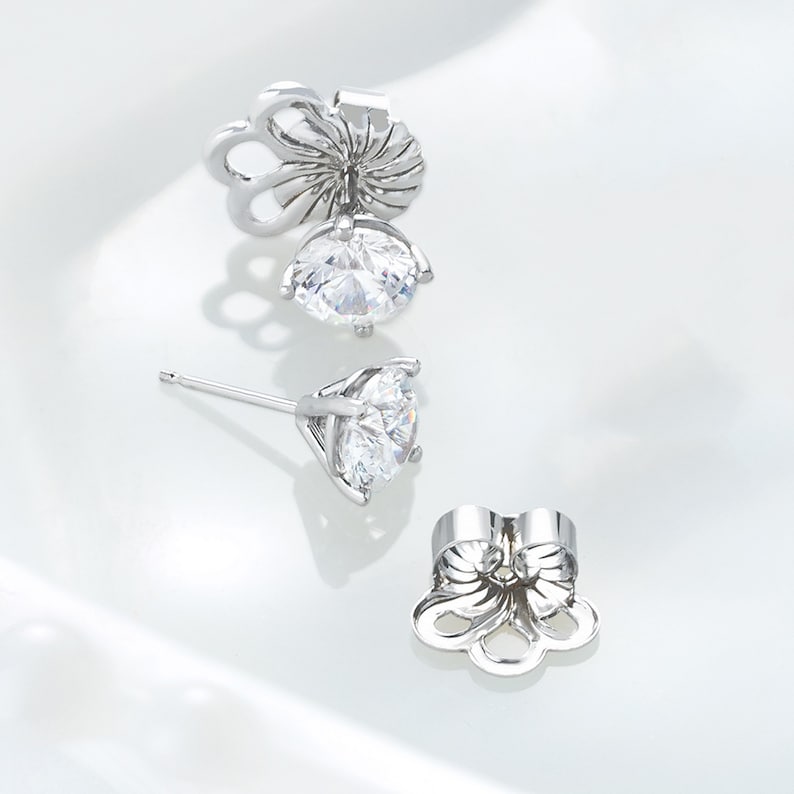 May include: A pair of silver stud earrings with a clear round stone. The earrings have a butterfly-shaped back.
