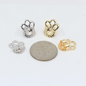 May include: Four earring backs, two gold and two silver, shown next to a US dime for size comparison.