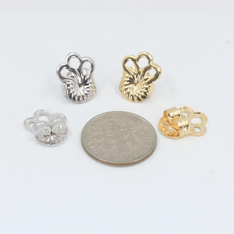 May include: Four earring backs, two gold and two silver, shown next to a US dime for size comparison.