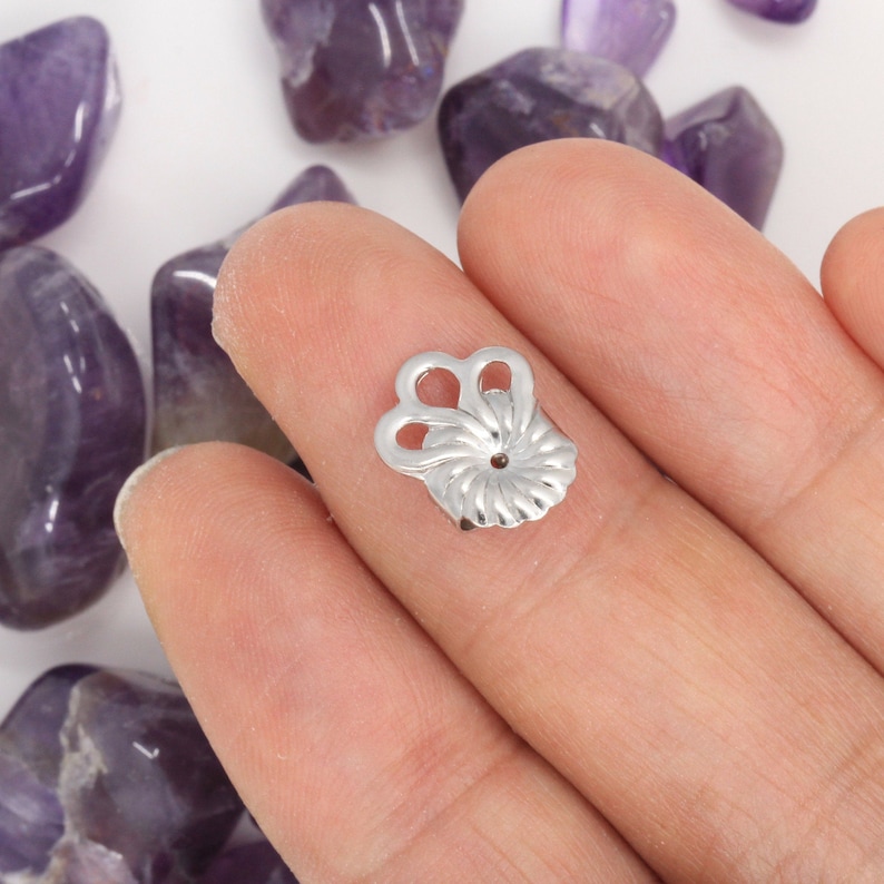 May include: Silver metal earring finding with a decorative design. The finding has a small hole in the center for attaching an earring.
