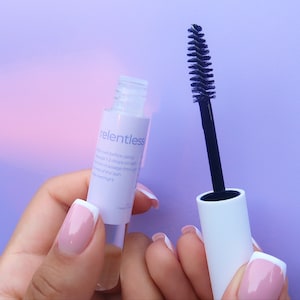 May include: A clear bottle with a white label that says "relentless" and a black mascara wand with a white cap. The bottle and wand are both on a purple background.