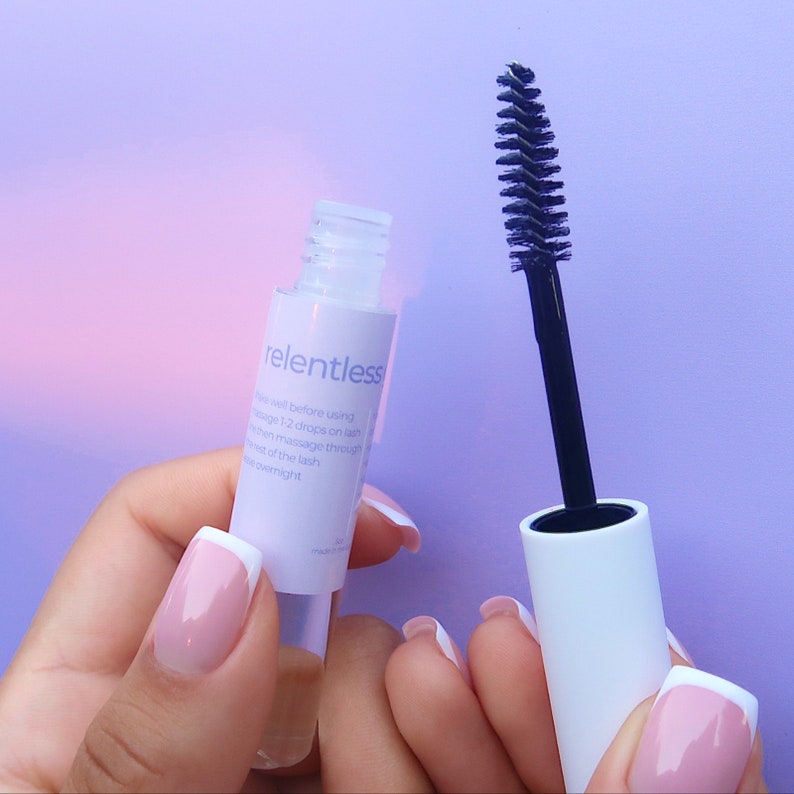 May include: A clear bottle with a white label that says "relentless" and a black mascara wand with a white cap. The bottle and wand are both on a purple background.