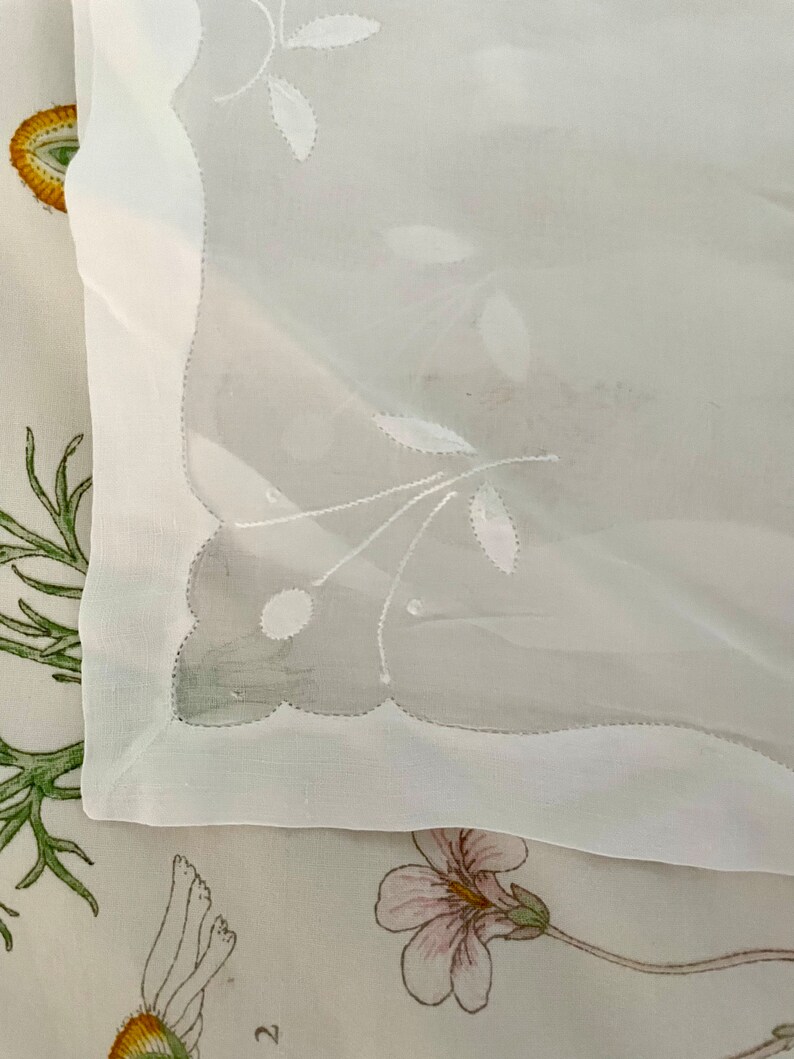 Pode incluir: Toalha de mesa branca transparente com delicados desenhos florais bordados. A toalha de mesa tem uma borda festoneada e &eacute; feita de um tecido leve.