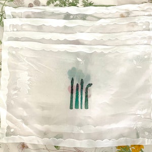 Pode incluir: Conjunto de seis guardanapos de mesa de renda branca com um desenho bordado de espargos.