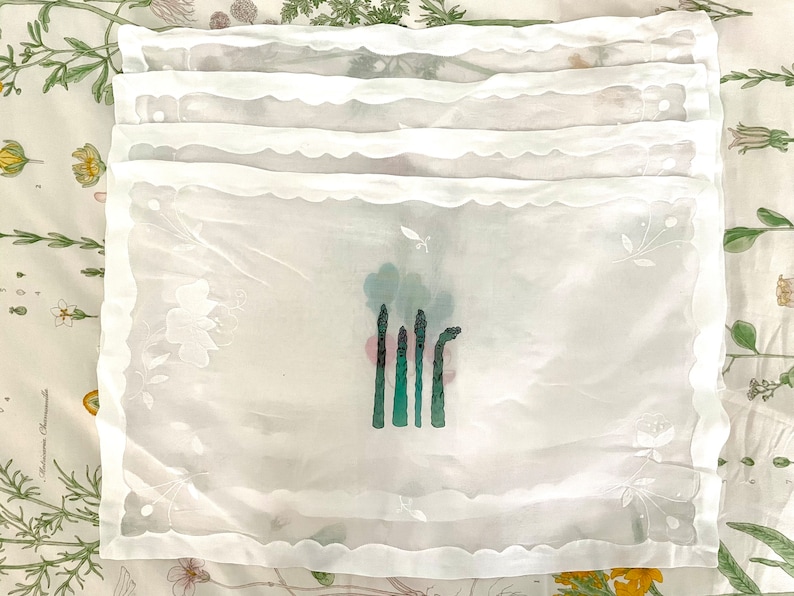 Pode incluir: Conjunto de seis guardanapos de mesa de renda branca com um desenho bordado de espargos.