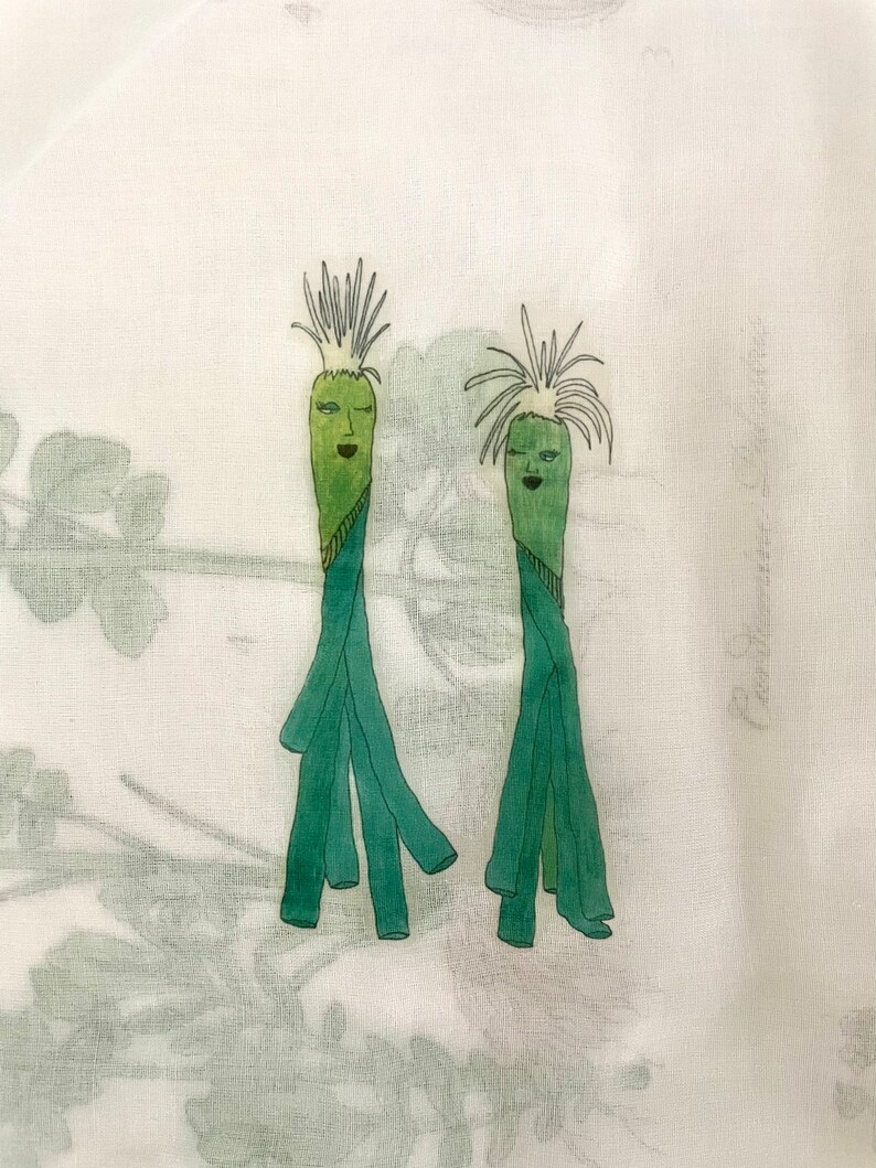 Pode incluir: Duas figuras de desenho animado verdes com rostos e cabelos, desenhadas em um fundo de tecido branco.