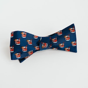 May include: A navy blue bow tie with a pattern of red cocktails. The bow tie is made of silk and has a classic design.