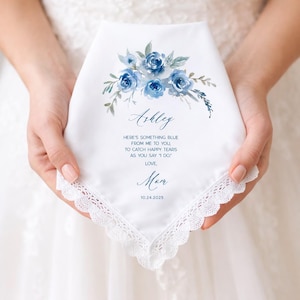 May include: White handkerchief with a blue floral design and lace trim. The handkerchief has the name "Ashley" and the text "HERE'S SOMETHING BLUE FROM ME TO YOU, TO CATCH HAPPY TEARS AS YOU SAY 'I DO' LOVE, Mom 10.24.2025."