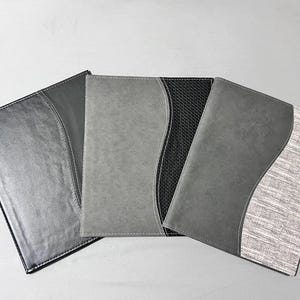 Könnte beinhalten: Drei graue Dokumentenhalter mit geschwungenen Akzentdesigns. Die Halter haben verschiedene Texturen, darunter glatt, strukturiert und ein gewebter Stoff. Die Halter sind in Grau- und Schwarztönen gehalten und eignen sich für Büro oder den persönlichen Gebrauch.