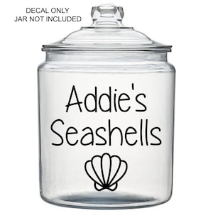 May include: A clear glass jar with a lid, featuring the text "Addie's Seashells" in black script, along with a seashell graphic. The text "DECAL ONLY JAR NOT INCLUDED" is above the jar. Ideal for storing seashells.