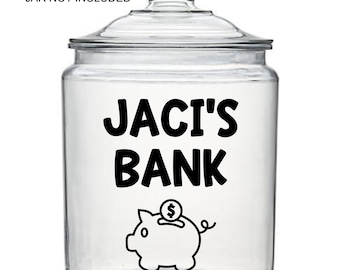 Op de afbeelding: Een doorzichtige glazen pot met deksel voorzien van een zwarte vinyl sticker met de tekst JACI'S BANK boven een afbeelding van een spaarvarken met een munt. De tekst DECAL ONLY JAR NOT INCLUDED staat in het zwart boven de pot.