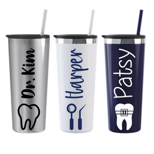Puede incluir: Tres vasos de acero inoxidable con diferentes dise&ntilde;os. El primer vaso es plateado con el texto "Dr. Kim" y un gr&aacute;fico de diente. El segundo vaso es blanco con el texto "Harper" y un gr&aacute;fico de herramienta dental. El tercer vaso es azul con el texto "Patsy" y un gr&aacute;fico de diente con brackets.