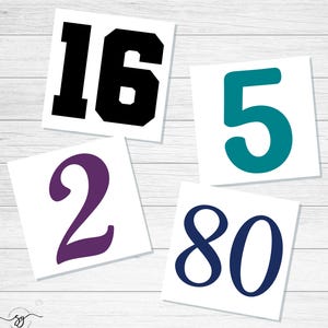 May include: Four white square cards with different numbers printed on them. The numbers are in various colors: black, teal, purple, and navy blue. The numbers are 16, 5, 2, and 80. The background is a light wood grain.
