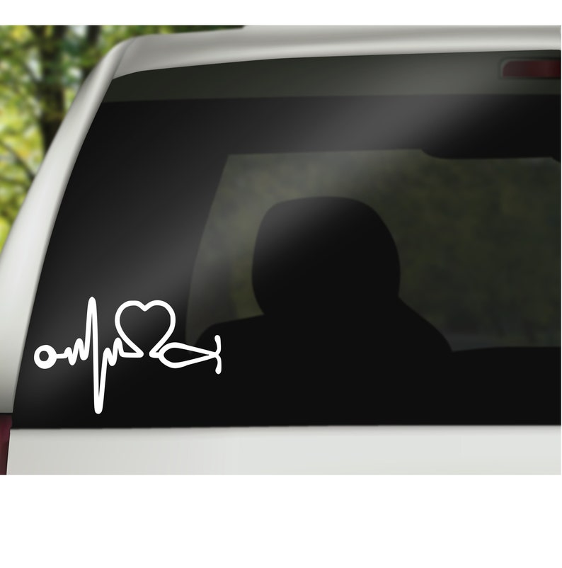 K&ouml;nnte beinhalten: Wei&szlig;er Vinyl-Aufkleber mit einem Herzen, einem Stethoskop und einer Herzschlaglinie. Der Aufkleber befindet sich auf der Heckscheibe eines Autos.