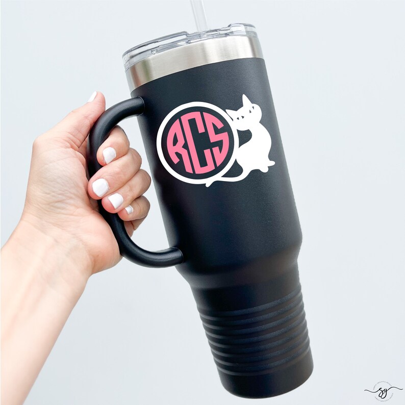 May include: Black stainless steel travel mug with a handle. The mug has a white cat sticker with a pink monogram circle that says "RCS" on it.