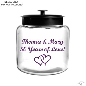 Op de afbeelding: Een doorzichtige glazen pot met een zwarte deksel en een paarse sticker met de tekst Thomas & Mary 50 Years of Love! en twee in elkaar grijpende harten. De afbeelding bevat de tekst DECAL ONLY JAR NOT INCLUDED.