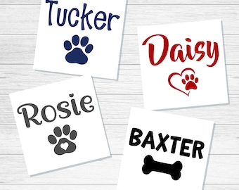 May include: Four square white decals featuring pet names and icons. One shows navy text Tucker with a paw print, one red text Daisy with a heart-shaped paw, one gray text Rosie with a heart-centered paw, and one black text BAXTER with a bone icon.