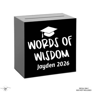 May include: A black graduation box with a slot on top. The front of the box features the words "WORDS OF WISDOM" in white, along with a graduation cap graphic and the name "Jayden 2026".
