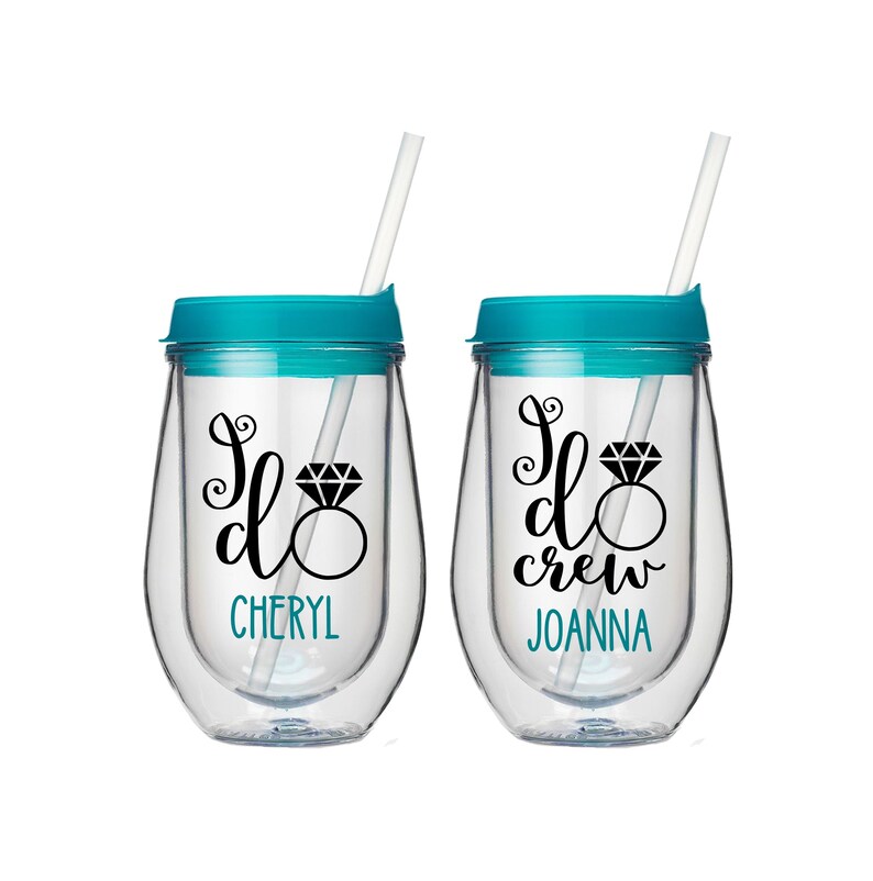 Pu&ograve; includere: Due bicchieri da vino in plastica trasparente con coperchi turchesi e cannucce. I bicchieri hanno scritte in vinile nero che dicono "I do" con un grafico di anello di diamanti e i nomi "Cheryl" e "Joanna" in basso. Il bicchiere a destra dice "I do crew".