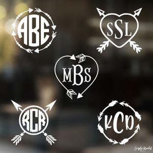 May include: Five white vinyl decal designs featuring monograms with letters ABE, SSL, MBS, RCR, and KCD. The designs incorporate circular or heart-shaped frames accented with arrow motifs, feathers, and decorative lines in a clean, graphic style.