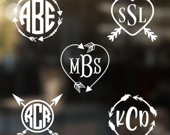 May include: Five white vinyl decal designs featuring monograms with letters ABE, SSL, MBS, RCR, and KCD. The designs incorporate circular or heart-shaped frames accented with arrow motifs, feathers, and decorative lines in a clean, graphic style.